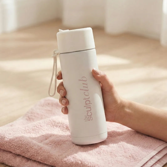 White water bottle with 'the sculpt club' branding held by a hand on a pink towel.